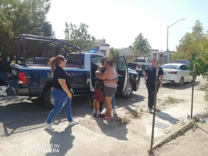 Madre abrazando a su hijo a un lado de una patrulla