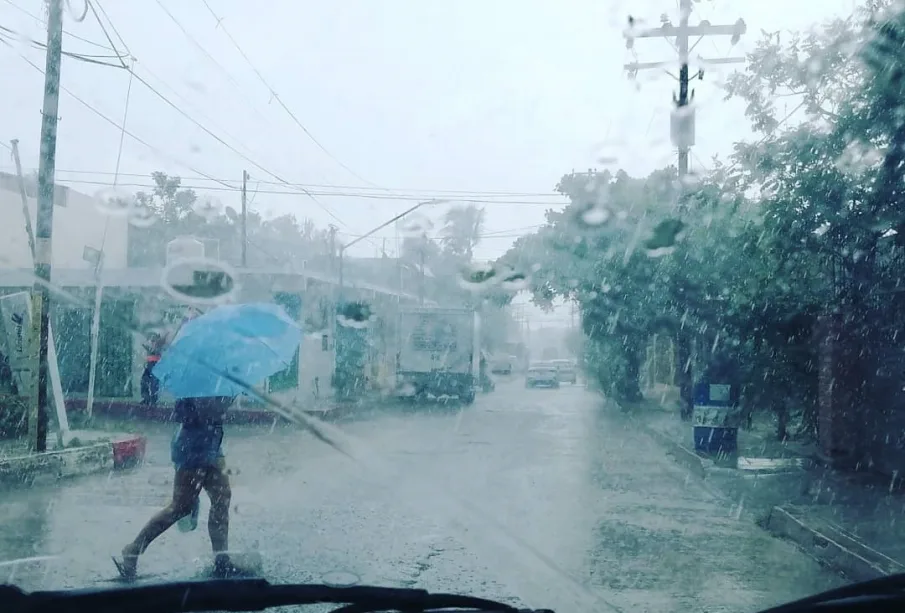 Persona cruzando calle bajo la lluvia protegiéndose con paraguas