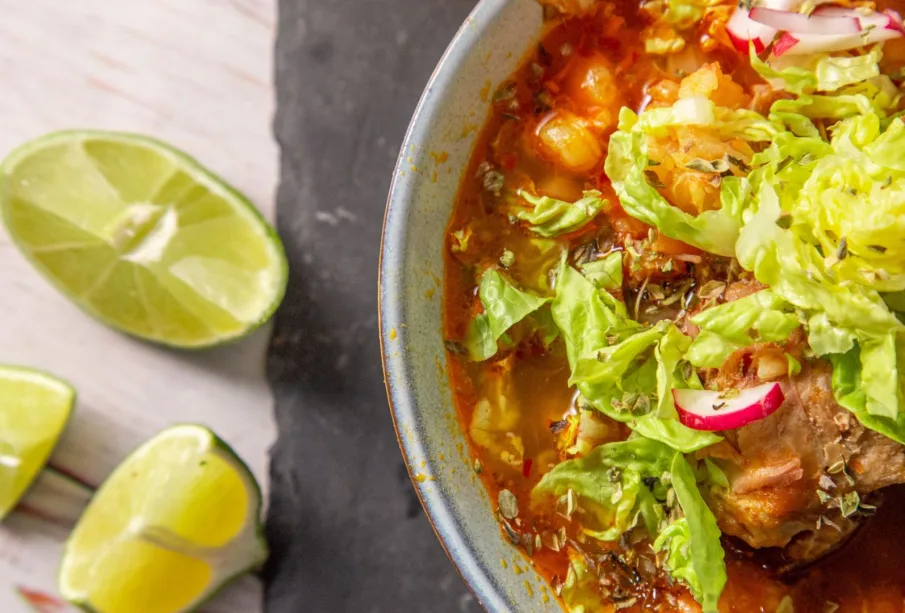 Plato de pozole rojo con limones