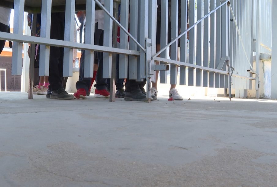 puerta de plantel cerrado con jóvenes afuera