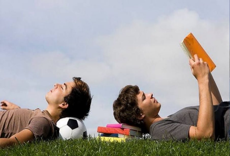 Adolescente leyendo y otro acostado sobre un balón