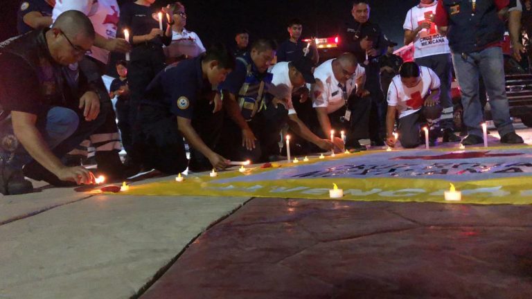 Integrantes de Bomberos y Cruz Roja encendiendo velas en conmemoración