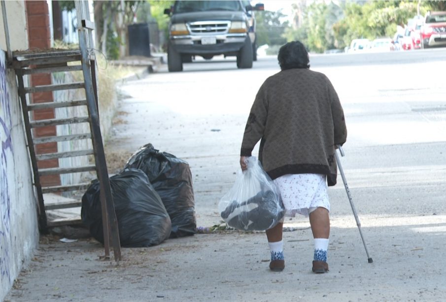 Señora de la tercera edad caminando con bolsa y bastón en mano