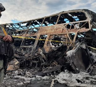 Soldado resguardando restos de autobus y tráiler incinerado