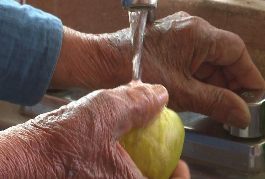 Manos lavando una manzana con agua contaminada