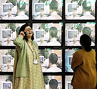 A woman talks on her cell phone as another stares at a multi-screen display at 'IT Asia 2000', an IT expo,which began in New Delhi on Tuesday.   AFP