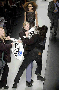 A videographer tries to pull a sign away from anti-fur protesters after they jumped onto the runway during the presentation of Oscar de la Renta�s Fall 2000 show, Tuesday, at Bryant Park in New York