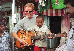 South African cricketer Shaun Pollock plays the guitar with the child of a sex worker during a visit to Bombay's notorious Kamatipura red-light