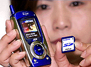 Matsushita employee Toshie displays a gadget which can download digital music contents through a mobile phone network and store the contents on a stamp-sized IC memory SD card. 