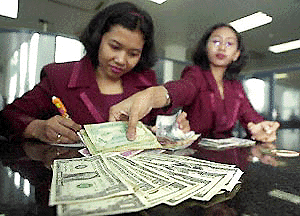 Indonesian tellers place US dollars in exchange for rupiah notes on the counter at a money changer in Jakarta on Thursday. Indonesia blamed political factors for the weakening of the currency