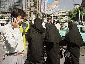 An Iranian uses his mobile phone in Tehran on Thursday as burqa-clad women pass by. Thousands of Iranians are besieging their local post office to buy mobile telephone lines, both for themselves and in the expectation of re-selling them at a handsome profit when they come into service in a year's time