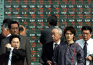 Passers-by stand in front of an electronic stock price board in downtown Tokyo on Monday. Share prices closed 2.8 per cent lower on massive selling on high-technology issues in response to heavy falls on Wall Street at the end of last week