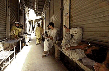 Labourers take rest in the shadows of downed shutters at a market in Rawalpindi city, some 25 km from Islamabad, on Monday. All major markets were closed as traders observed a strike against the national tax survey launched by the military regime. � AFP