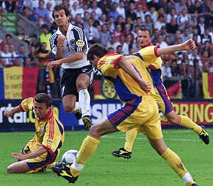 Germany's Mehmet Scholl jumps over Romanian Dan Petrescu (ground) as Liviu Ciobotariu (R) tries to reach the ball during their European Championship group A match in Liege on Monday