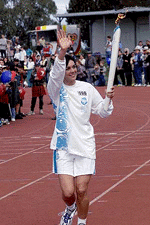 Australian swimmer Sam Riley, holding the Olympic torch, waves to the crowd as she runs into a stadium in Nathan June 13