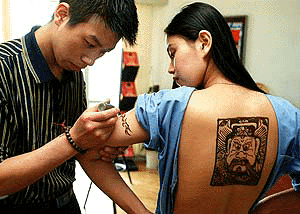 A body-painting worker tattoos various patterns with henna on a girl's arms and back in Shanghai on Thursday
