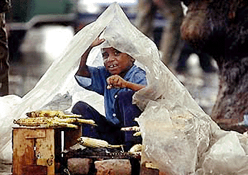 A young street-side corn vendor covers himself with a plastic sheet as he is caught in a monsoon downpour in New Delhi, 11 July 2000.  Heavy rains have been lashing the capital for the past two weeks causing minor flooding and traffic snares. 