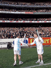 Australian soccer hero Paul Wade (left) exchanges flames with Olympian Ron Barassi on the pitch of the Melbourne Cricket Ground in Melbourne, Australia on Sunday