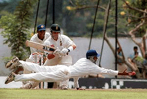 Sri Lankan fielder Rasal Arnold dives to hold a catch from South African batsman Mark Boucher (center) as wicket keeper Kumara Sanagkkara looks on during the first day of the second cricket test at Asgiriya International Cricket Ground in Kandy, Sri Lanka on Sunday