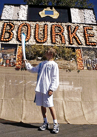 Cameron Liddell holds the Olympic torch in front of farm product display at Bourke, New South Wales on Sunday. The Olympic Torch is spending 100 days travelling around Australia on its way to Sydney for the opening ceremony of the Sydney 2000 Olympic Games on September 15