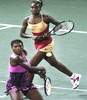 Venus Williams (R) watches as her sister Serena prepares to hit a return during their doubles match against Lilia Osterloh and Alexandra Stevenson at the US Open tennis tournament on Saturday