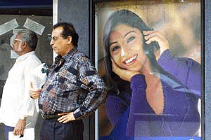 Commuters in Mumbai wait for a bus in front of an advertisement by a cellphone company on Friday. An ongoing protest by workers in the government-run telecom agency has crippled long-distance phone services across the country for days. Telecom employees are demanding job security when the agency is corporatised in October. -- Reuters Photo