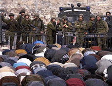 Israeli border guards watch Palestinians pray near a roadblock in the West Bank town of Bethlehem on Friday.