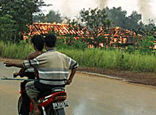 Dayak youths, carrying a spear, ride past a burning ethnic Madurese house near Palangkaraya on the island of Borneo on Sunday. 