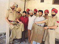Mr Santokh Singh, Station House Officer, Focal Point Police Station, shows the police uniforms that were seized from three members of a gang of automobile thieves who are also in the picture.