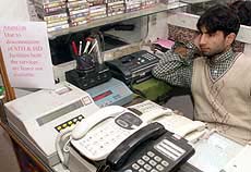 A Kashmiri PCO owner sits near a notice