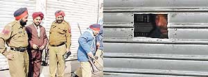 Police and excise officials monitor sealing of a liquor shop, and (right) a man peeps through an opening in a liquor vend which was sealed by the Excise Department.