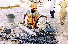 A tribesman in the process of fixing the bottom of an iron bucket.