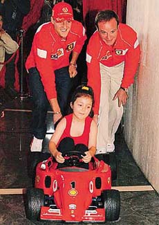 Germany's Michael Schumacher (L) pushes a miniature Ferrari car driven by five-year-old Teaghan Santamaria 