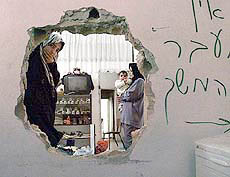 A Palestinian family looks through a hole in their house made by Israeli soldiers 