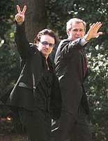 Bono, left, lead singer of the Irish rock group U2, gives the peace sign as he walks with President Bush on their return to the White House