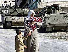 A Palestinian woman and her children pass Israeli tanks