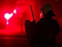 A Dutch policeman stands in front of a hooligan holding a flare