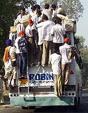 Schoolchildren along with other passengers hang on the back of an overcrowded bus