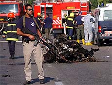 An Israeli security officer stands guard by the remains of a civilian car which earlier blew up 