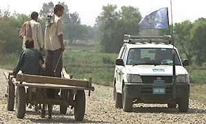 Villagers riding on horse cart look at a United Nations Military Observation Group vehicle