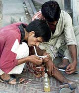 Two Pakistani drug users take drugs on a roadside in Lahore. 