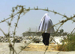 A Palestinian woman walks behind barbed wire