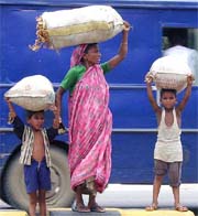 Two kids carrying load cross a road