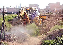 A JCB demolishes a wall constructed by a Punjab-based property dealer on the land belonging to Haryana in Sector 19, Panchkula-Baltana boundary, on Thursday.