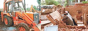 An earth mover damaged by angry residents of Madrasi Colony during a demolition drive in the colony, and (right) enforcement staff of HUDA demolish the temporary structures in the colony, near Nadda Sahib, in Panchkula on Tuesday. 