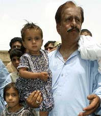 Two-year-old Ifra, being carried by her uncle, and five-year-old Iqra, look at journalists
