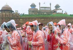 Indian schoolchildren wearing raincoats walk past Red Fort