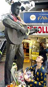 Japanese fan "Elovis" Sato places a hamburger on a bronze statue