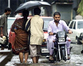 Pedestrians and a motorcyclist make their way through a water-logged street 