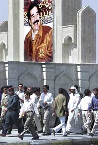 Iraqi people walk in front of a large picture of President Saddam Hussein